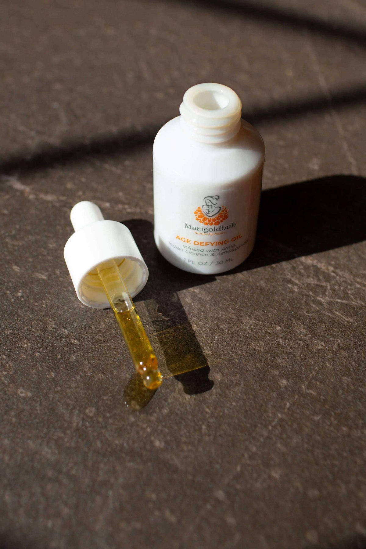 Age Defying Face Oil in a white bottle with a white dropper and visible golden amber oil in the glass pipette