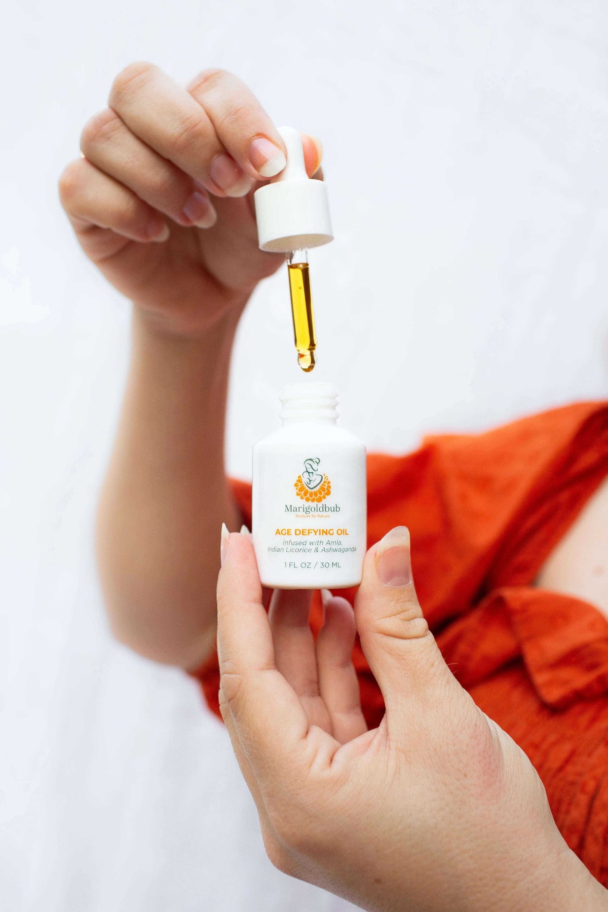 Age Defying Face Oil in a white glass dropper bottle, with golden oil visible in the pipette and an orange label