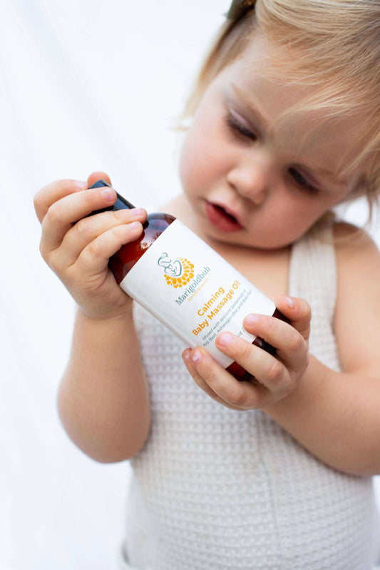 Calming Baby Massage Oil in a clear bottle with a black cap and white label featuring orange and blue print