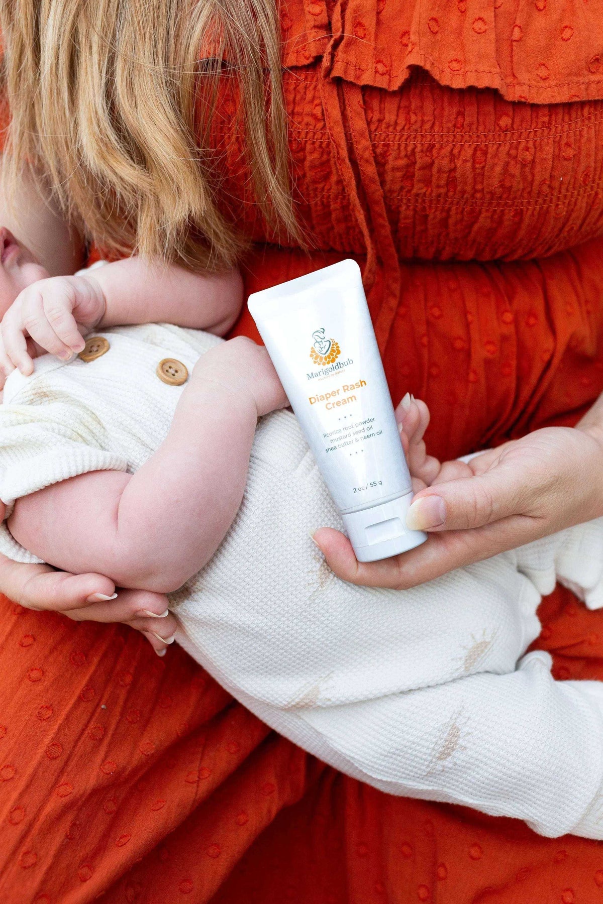 Diaper Rash Cream in a white squeeze tube with orange and gold label, held beside a baby in a white outfit