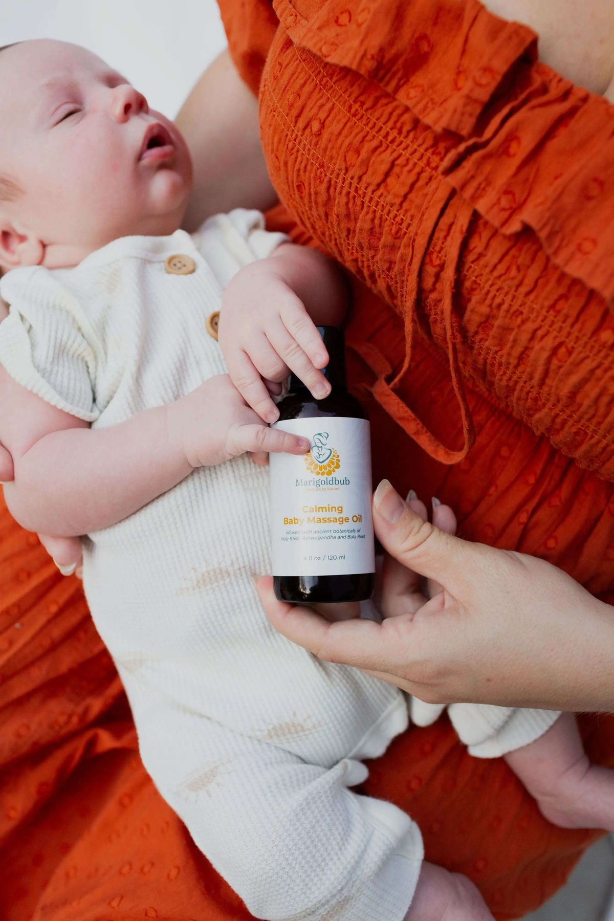 Gentle Beginnings - Baby Bundle with a newborn beside a hand-held amber bottle of calming baby massage oil