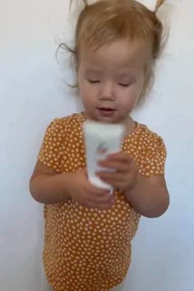 Gentle Beginnings - Baby Bundle features a toddler in a mustard floral romper holding a white skincare bottle