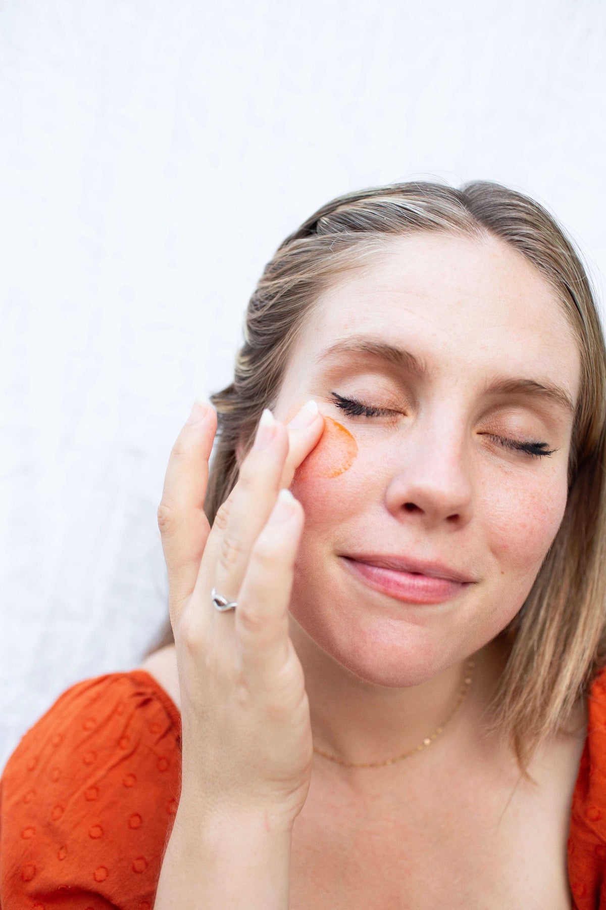 Illuminating Face Serum applied to a woman's cheek, shown as a small orange-tinted streak on skin