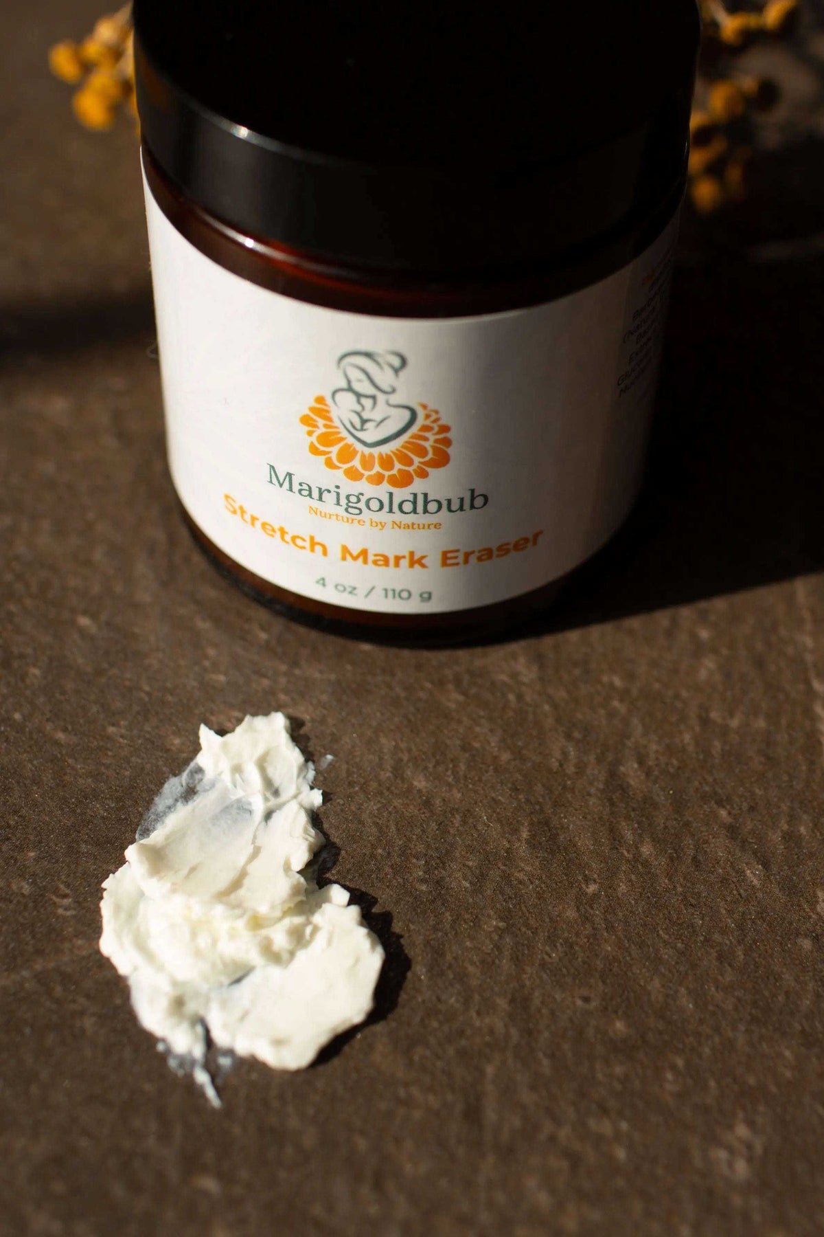 Stretch Mark Eraser moisturizer in a white jar with a dark lid, shown with a scoop of thick white cream